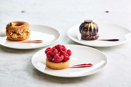 set of desserts raspberry tart on a white plate on a table with berry desserts, close up, side view. Set of four plates with desserts.の写真素材