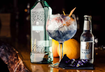 Gin and tonic served in a glass with orange zest on a table with gin bottle and tonic water side view. Gin tonic alcoholic cocktail with ice and mint. Cocktail drinks served at restaurant, pub or bar.の写真素材