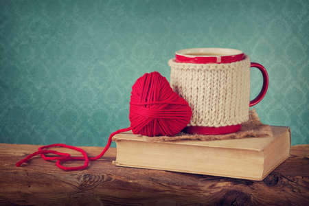 Cup of coffee standing on an old book and wool heartの写真素材