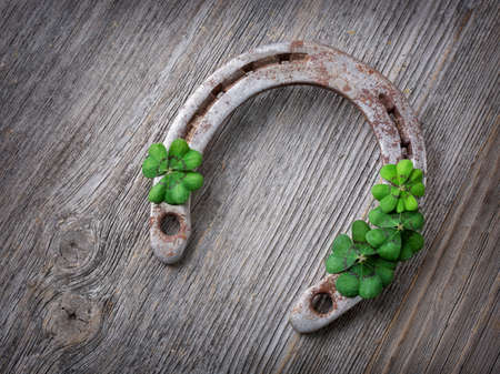 Old rusty horseshoe and four leaf clover on a wooden backgroundの写真素材