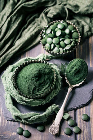 Spirulina tablets and powder in bowls on a wooden backgroundの写真素材
