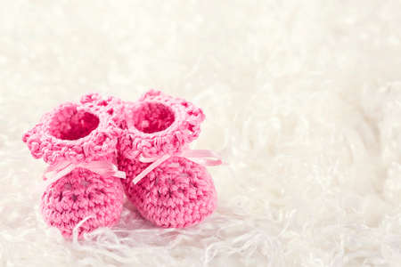 Pink baby crochet shoes on a white furの写真素材