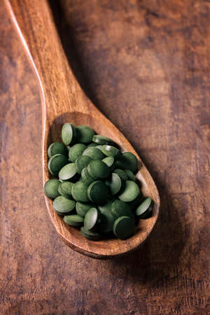 Spirulina tablets in a spoon on a wooden backgroundの写真素材