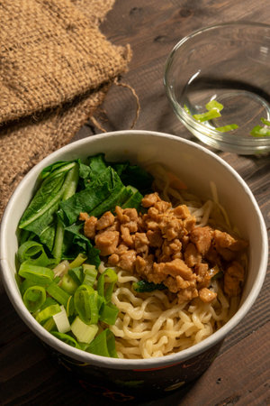 Chicken noodles in white bowl and wooden chopsticks on natural background with chicken pieces, green mustard, sauce. Indonesian Chicken Noodlesの写真素材