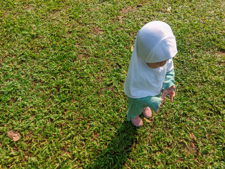 a small child wearing a hijab is standing on green grass with the morning sunの写真素材
