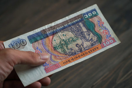 Hand holding kyats currency with face value 100 kyats on dark brown textured wooden background. Soft focus, selective focusの写真素材