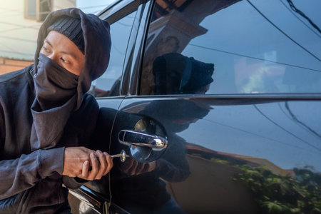 Car thief in mask tries to open car door with screwdriver. The thief tries to break the car window door.の写真素材