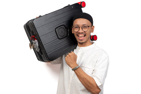 Asian Muslim man clenches fist showing excitement when carrying suitcase. The concept of returning home (Mudik)の写真素材