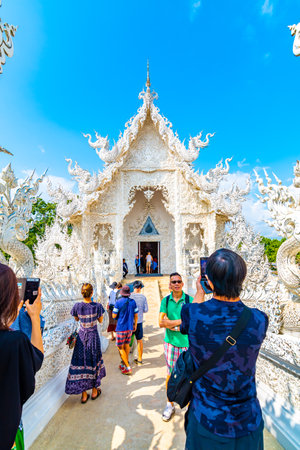 CHIANG RAI, THAILAND - 6.11.2019: Tourists visit famous white temple (Wat Rong Khun) near Chiang Rai city. White temple with bridge above damned souls of sinners, path to the heaven. Blue sky.のeditorial素材