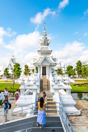 CHIANG RAI, THAILAND - 6.11.2019: Tourists visit famous white temple (Wat Rong Khun) near Chiang Rai city. White temple with bridge above damned souls of sinners, path to the heaven. Blue sky.のeditorial素材