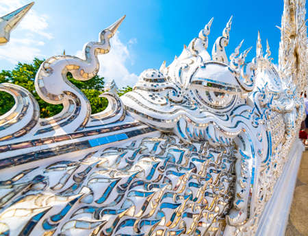 The white temple (Wat Rong Khun) in Chiang Rai city, Thailand. Beautiful buddhist ancient building with bridge above damned souls of sinners, path to the heaven. Famous tourist destination. Blue sky.の写真素材