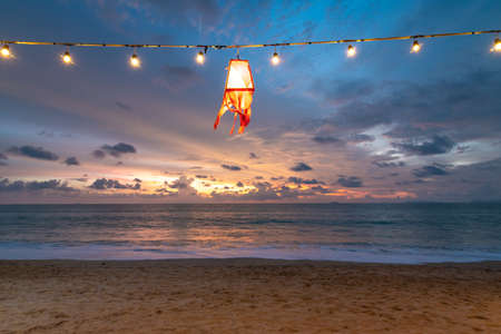 The red beach lantern lamp is hanging on cable with lightbulb. Beach lighting equipment near the sea...