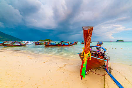 Small harbor with long tail boats at Ko Lipe island, Thailand, shortly before tropical storm. Big and heavy dark clouds above sea. Detail of wooden boats typical for Thailand.の写真素材