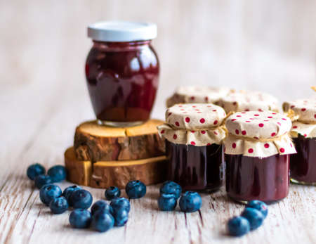Blueberry jam placed in small glasses on wooden desk. Fresh blueberries around. Homemade marmalade, concept of healthy cooking.の写真素材