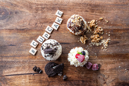 Three tasty cupcakes placed on wooden desk. White creme, chocolate and raspberry, covered with nut. The word cupcake made from wooden blocks.の写真素材