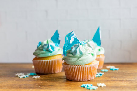 Homemade cupcake of blue color placed on wooden desk. Winter and christmas theme, snowflakes on cream with blue ice. Fresh and home baked sweet.の写真素材