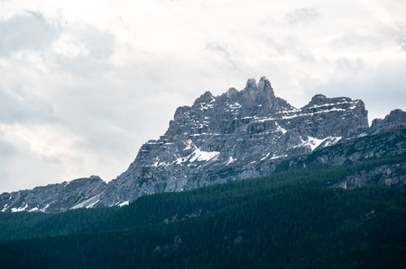 A panoramic view of the Dolomites, with towering mountains and clouds in the background. In the foreground, lush trees and dense forests create a vibrant contrast against the rugged peaksの写真素材