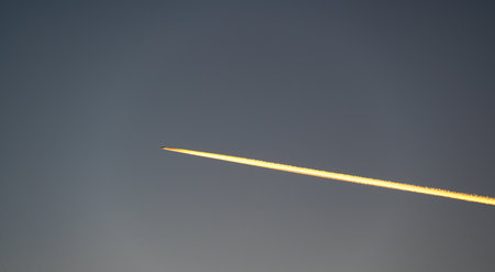 A stunning sunset view of a flying airplane, captured from the ground, with fiery condensation...