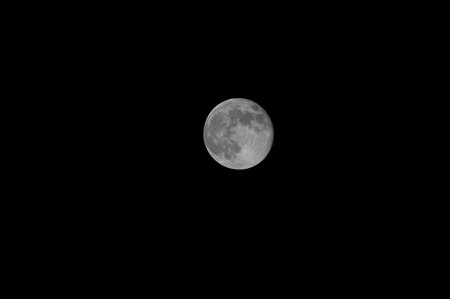 A close-up shot of the full moon captured through a telephoto lens, revealing its surface with visible craters, showcasing the moon's detailed and captivating featuresの写真素材