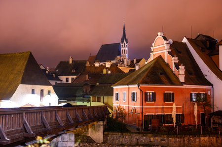 A panoramic night view of Cesky Krumlov, showcasing the rooftops, illuminated buildings, and the Church of St. Vitus beautifully lit up against the dark skyの写真素材