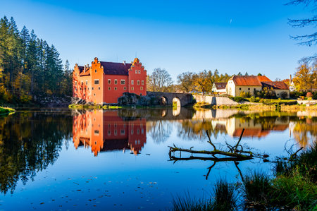 Panoramic view of Cervena Lhota Castle in the Czech Republic, surrounded by a lake reflecting its image. Autumn trees in vibrant colors and sunny weather create a picturesque, serene scene.の写真素材