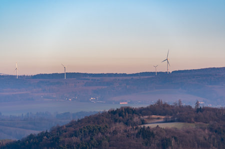 Wind turbines stand tall on rolling hills during a stunning sunset. The sky transitions from deep blue to vibrant shades of purple and red, creating a dramatic and peaceful sceneの写真素材