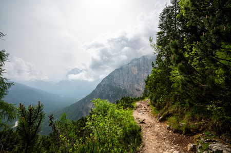 Mountain trail in the Dolomites (Dolomiti, Dolomiten), Italy, leading to Lago Sorapis. The path winds along rocky slopes with stunning views of valleys, forests, and peaksの写真素材
