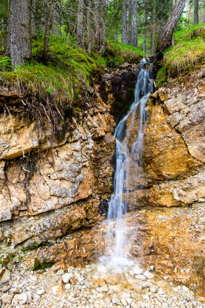 Small waterfall cascading down a rocky cliff in a lush forest of the Dolomites (Dolomiti, Dolomiten), Italy. The fresh water flows over moss-covered stones in natureの写真素材