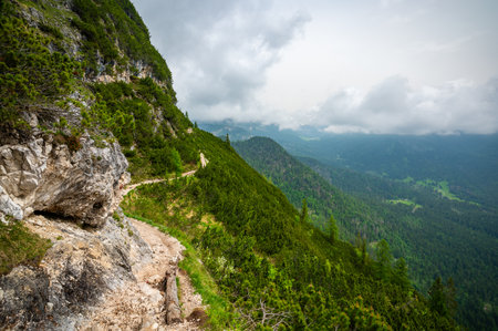 Mountain trail in the Dolomites (Dolomiti, Dolomiten), Italy, leading to Lago Sorapis. The path winds along rocky slopes with stunning views of valleys, forests, and peaksの写真素材