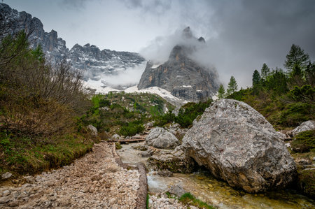 Rocky hiking trail near Lago Sorapis in the Dolomites (Dolomiti, Dolomiten), Italy. The path runs alongside a small mountain stream, with massive boulders and peaks in the backgroundの写真素材