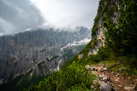 Mountain trail in the Dolomites (Dolomiti, Dolomiten), Italy, leading to Lago Sorapis. The path winds along rocky slopes with stunning views of valleys, forests, and peaksの写真素材