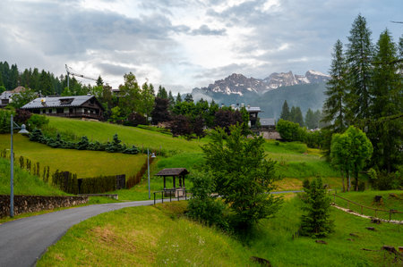 Scenic mountain village in the Dolomites (Dolomiti, Dolomiten), Italy. Cozy alpine houses on green slopes, towering peaks above, and clouds rolling through the valley belowの写真素材