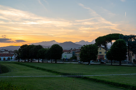 Sunset over the city of Lucca, Tuscany, viewed from the historic walls. The sun sets behind the Tuscan hills, casting a golden glow over rooftops and the peaceful landscape.の写真素材