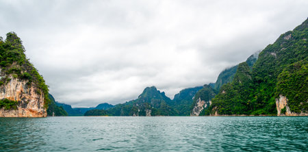 View of Khao Sok Lake in Krabi province, Thailand, with towering limestone cliffs covered in tropical rainforest rising above the calm surface of the lake.の写真素材