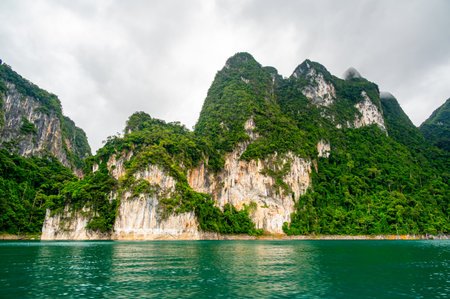 View of Khao Sok Lake in Krabi province, Thailand, with towering limestone cliffs covered in tropical rainforest rising above the calm surface of the lake.の写真素材