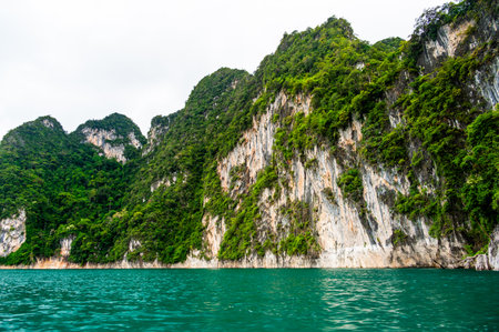 View of Khao Sok Lake in Krabi province, Thailand, with towering limestone cliffs covered in tropical rainforest rising above the calm surface of the lake.の写真素材