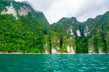 View of Khao Sok Lake in Krabi province, Thailand, with towering limestone cliffs covered in tropical rainforest rising above the calm surface of the lake.の写真素材