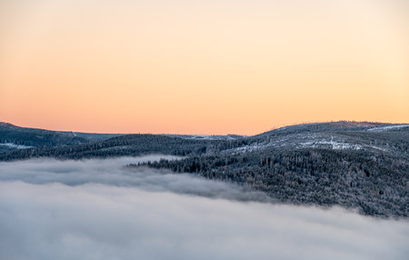 Winter inversion sunset with snow covered hills and forests rising above a sea of clouds, captured...