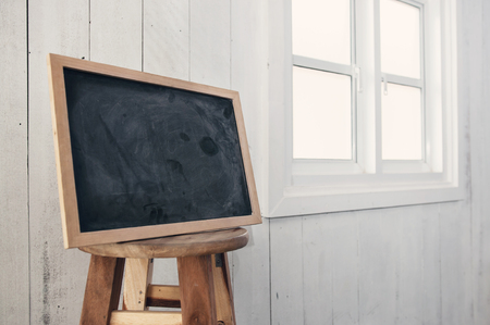 Foreground dirty chalkboard on round wooden chair,  near a white windowsill and white wooden wall background.の写真素材