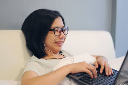 Asian woman be happy and smile with her laptop on a bed in her room.の写真素材
