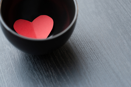 A red heart is in a bowl on grey wood background.の写真素材