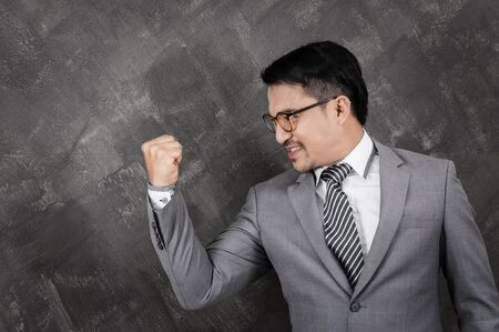 Successful businessman celebrating with arm up on grey background texture.の写真素材