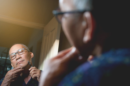 Old man is shaving the beard in the bathroom, Mirror reflect an asian old man is shaving beard.の写真素材