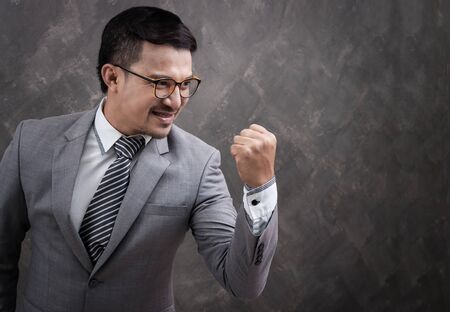 Successful businessman with an arm up on grey background texture.の写真素材