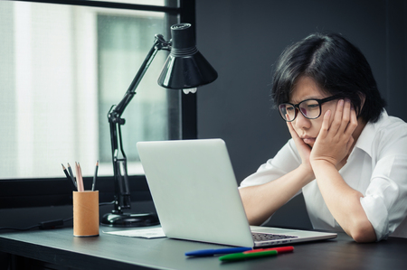 Close up of asian girl thinking about her work. Portrait of stressed young business woman in office. Exhausted and tired of business woman.の写真素材