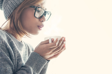 Winter and chistmas holidays concepts, Asian girl in woollen clothing with a cup of hot drink near a windowsill.の写真素材