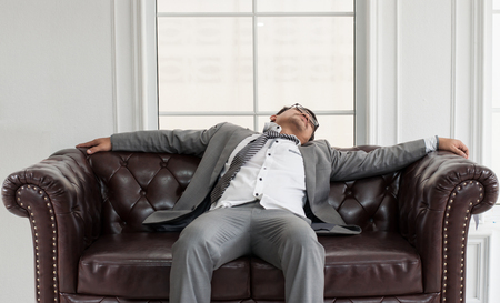Businessman exhausted and tired from overtime working, He sit and sleep on brown leather sofa.の写真素材