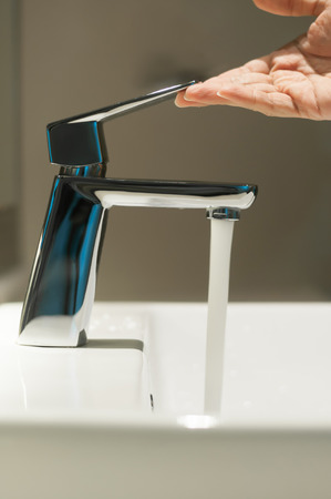 Close up of Hand with faucet and water flow on vanity basin in the bathroom.の写真素材
