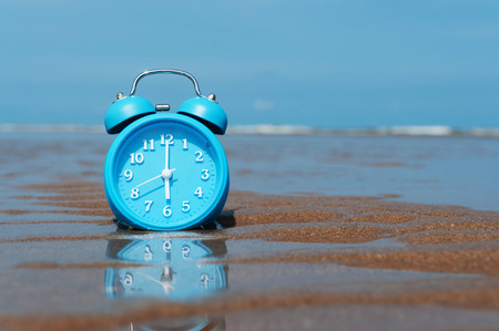 Retro alarm clock on sea and sand beach  background with reflection between sea and the alarm clock. Copyspaceの写真素材