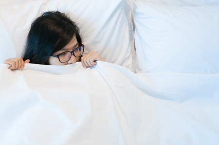 Beautiful asian woman wear eyeglasses waking up and looking to her bed.の写真素材